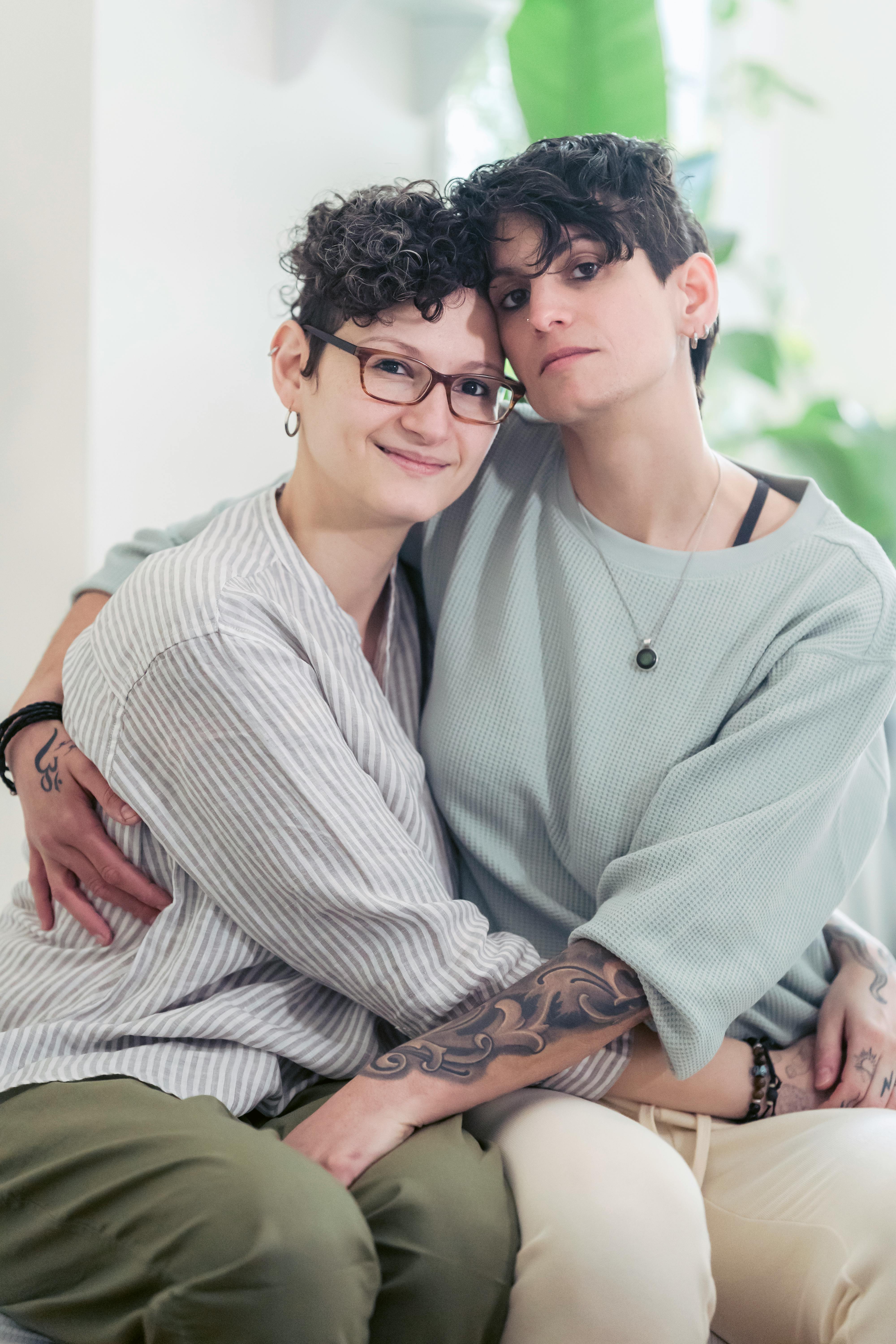 lesbian couple with tattoos embracing in house