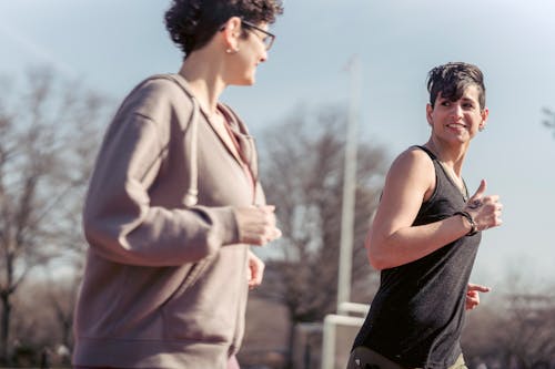 Free Cheerful active female friends in sportswear looking at each other while running on sunny street together during training in city Stock Photo