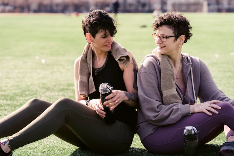 Positive Women In Sportswear Sitting On Lawn