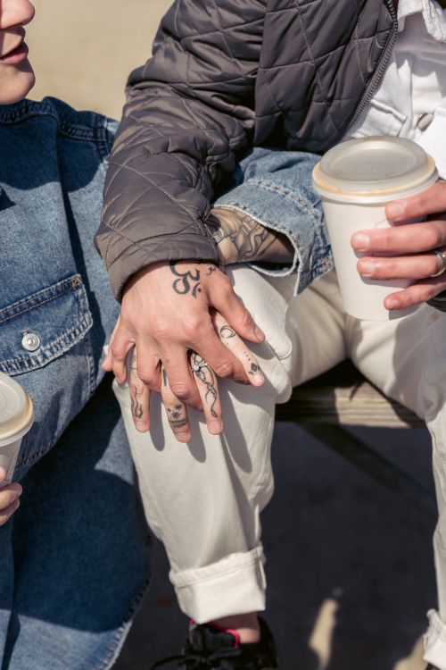 Free Crop anonymous tattooed romantic couple with cup of takeaway drinks holding hands while sitting together on sunny street in city Stock Photo