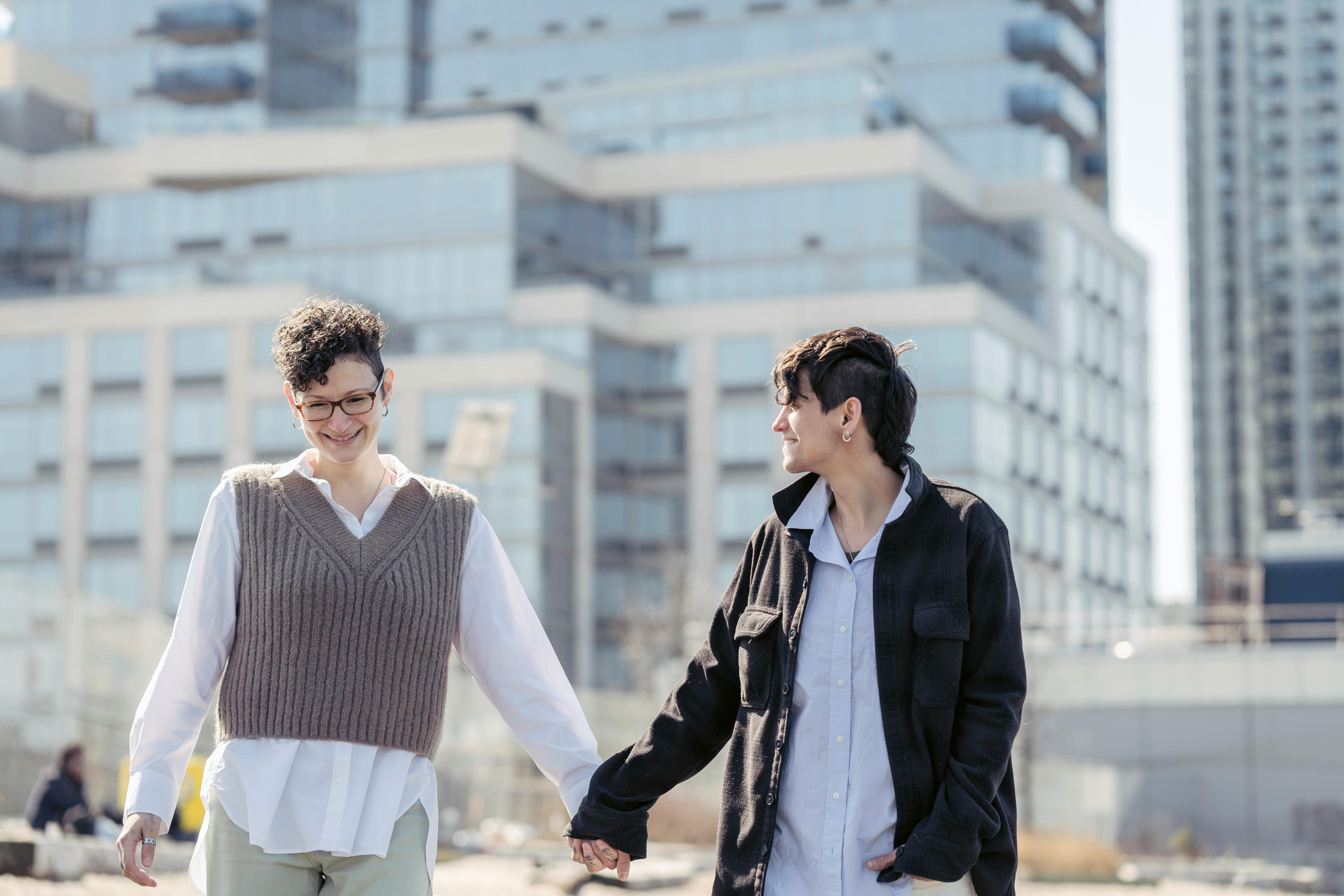 cheerful young homosexual women holding hands and walking in city