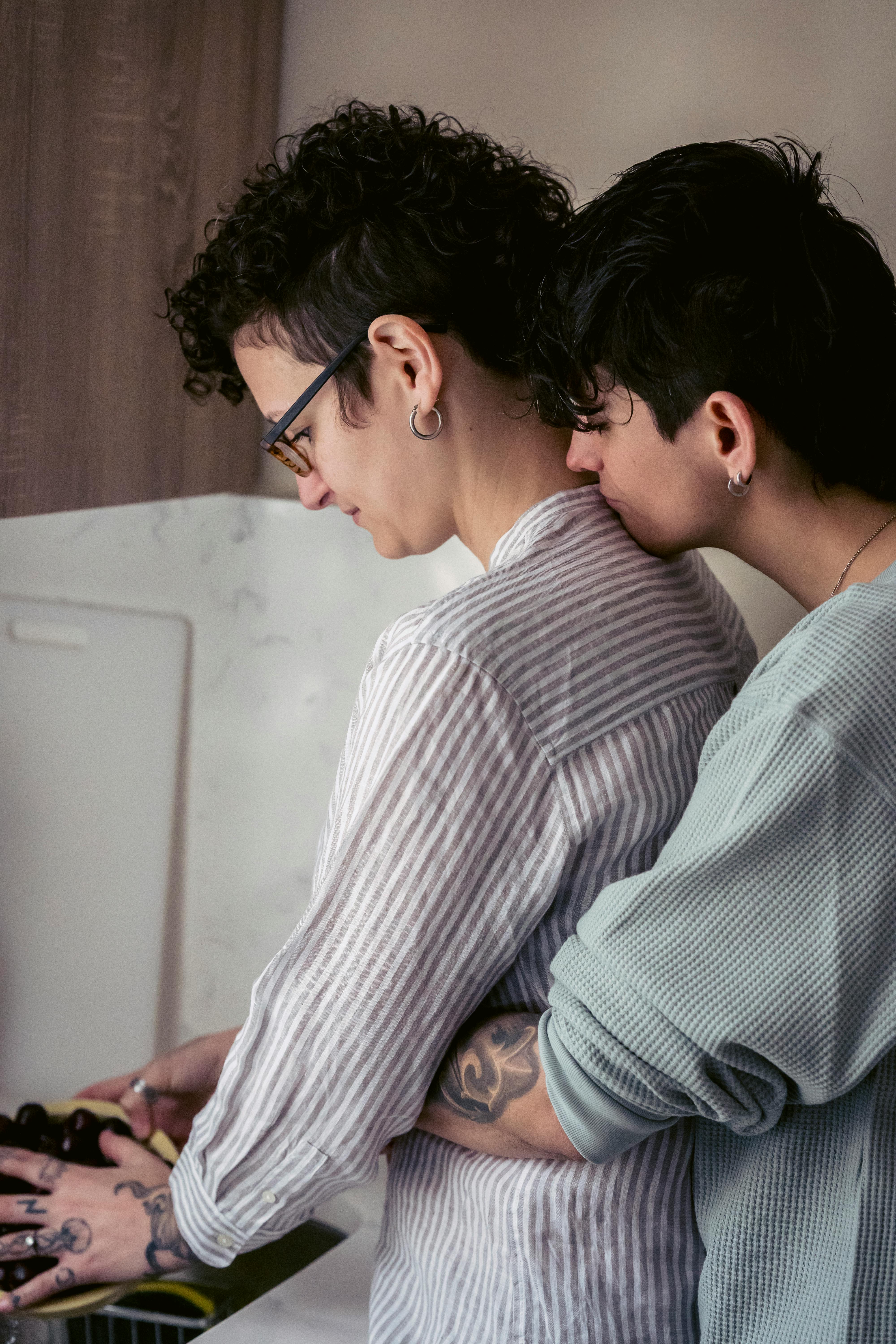 young homosexual lady embracing girlfriend washing berries in kitchen