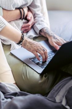 Close-up of tattooed hands typing on a laptop, showcasing personal style and technology interaction.