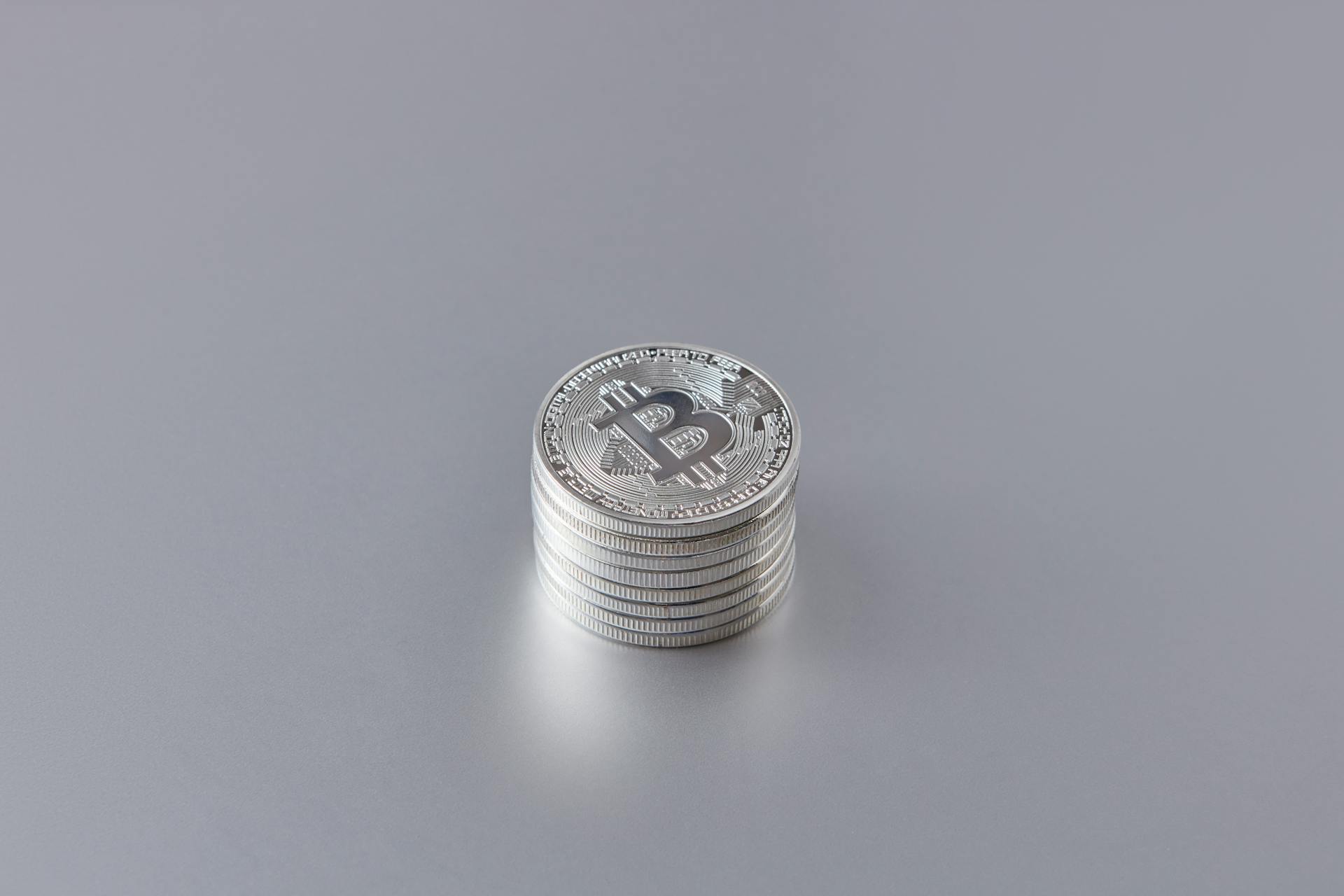 Close-up of silver Bitcoin coins stacked on a gray surface, showcasing cryptocurrency technology.