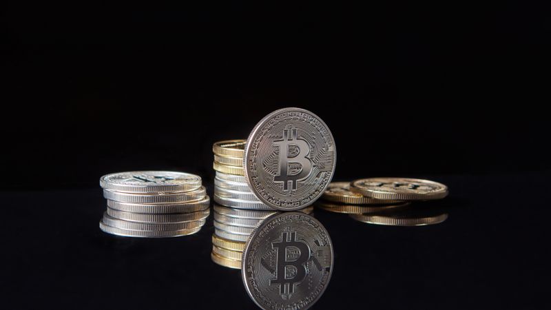 Silver bitcoins stacked on a reflective surface with a dark background, symbolizing cryptocurrency and digital wealth.