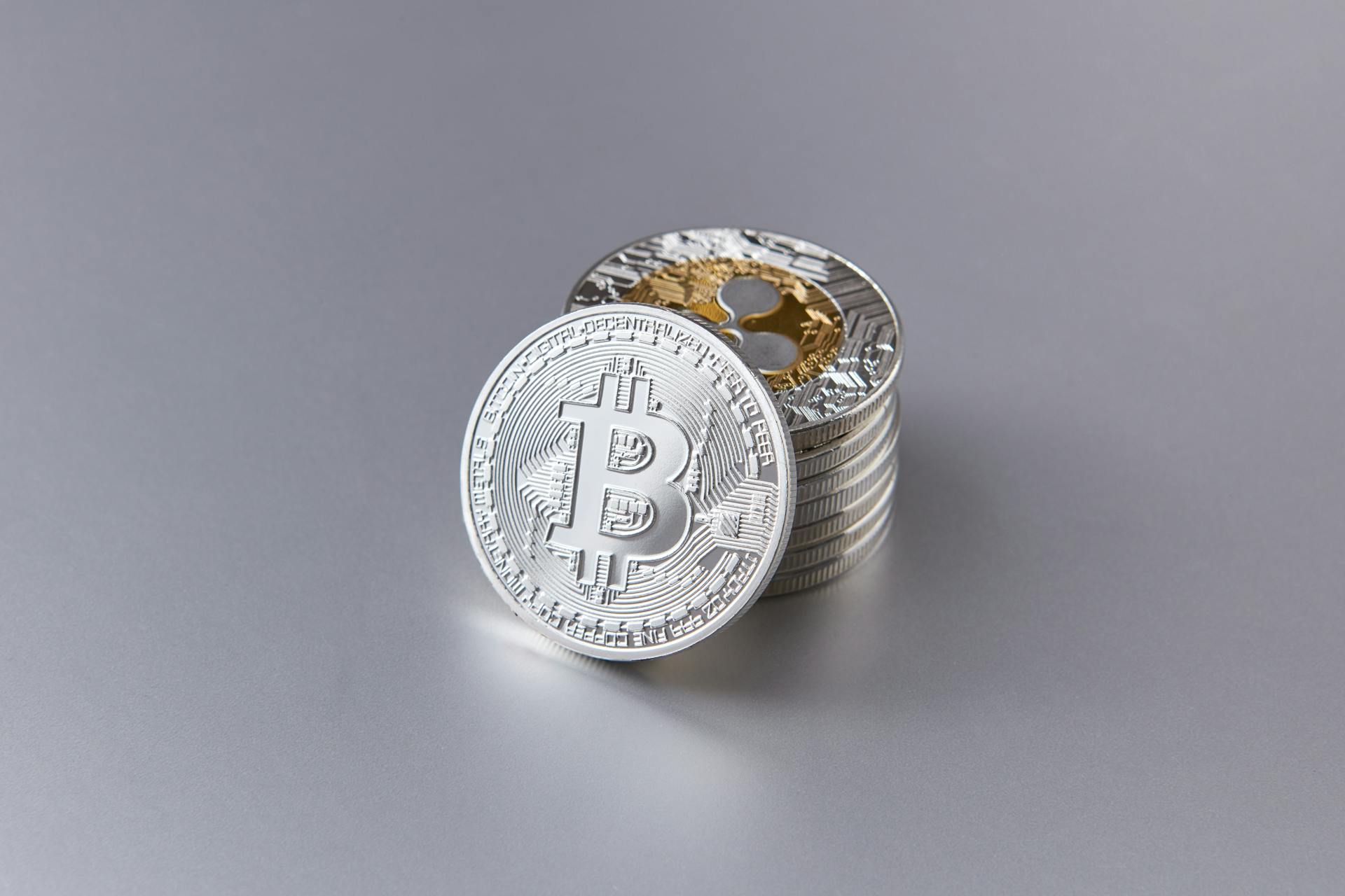 Close-up of shiny Bitcoin cryptocurrency coins with a reflective surface on a gray background.