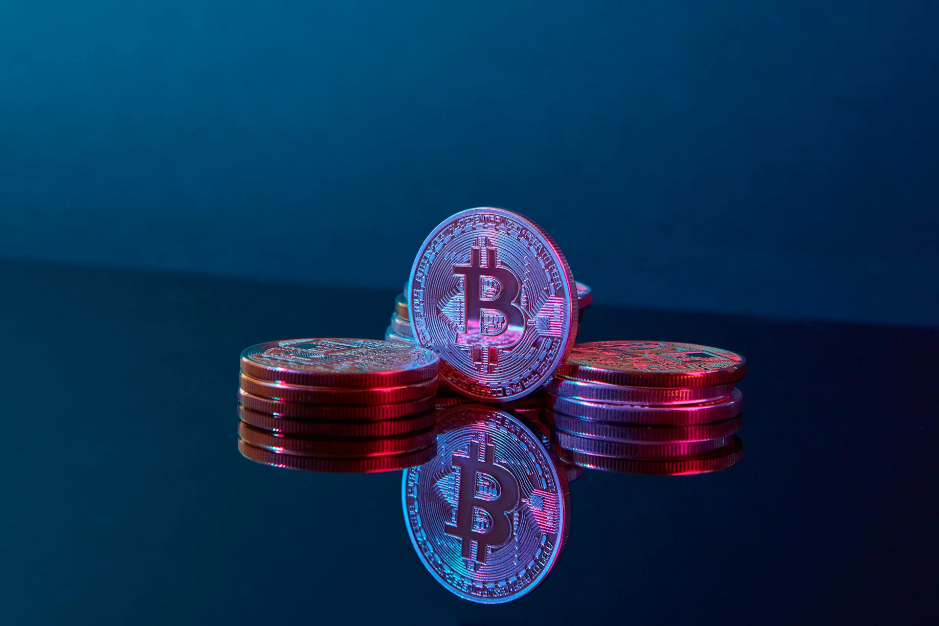 Stacked bitcoin coins on a reflective surface with a vibrant digital glow, symbolizing wealth and cryptocurrency.