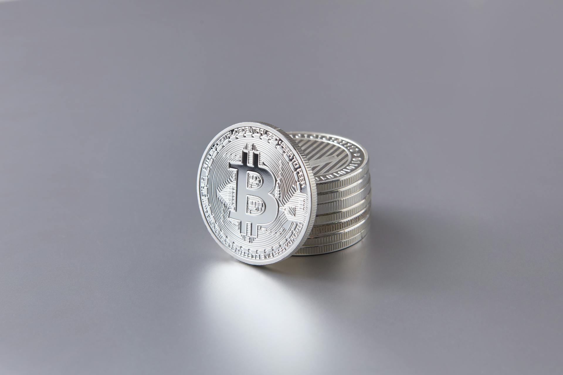 Stack of silver Bitcoin coins on a smooth gray surface, representing digital currency.