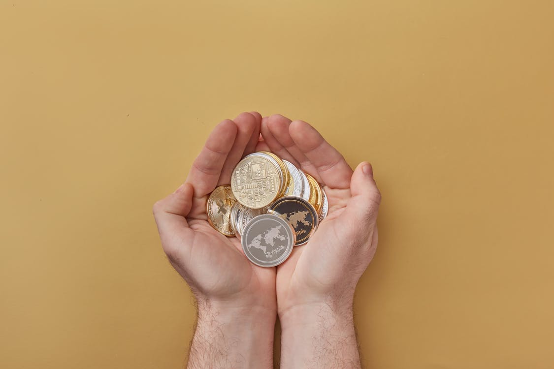 Pair of hands cupping assorted gold and silver collector coins against a yellow background