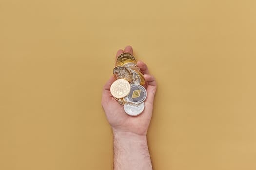Close-up of a hand holding various cryptocurrency coins against a yellow background.