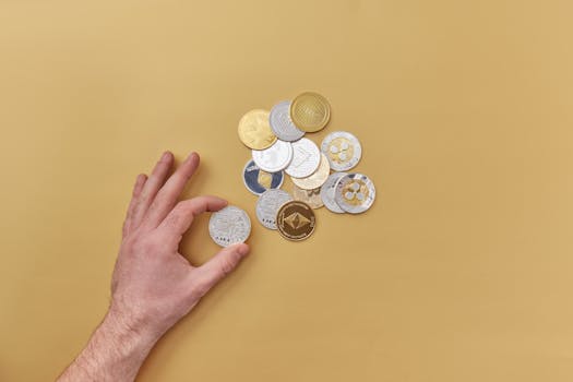 A hand picks cryptocurrencies from a mix of gold and silver coins on a vibrant yellow background.