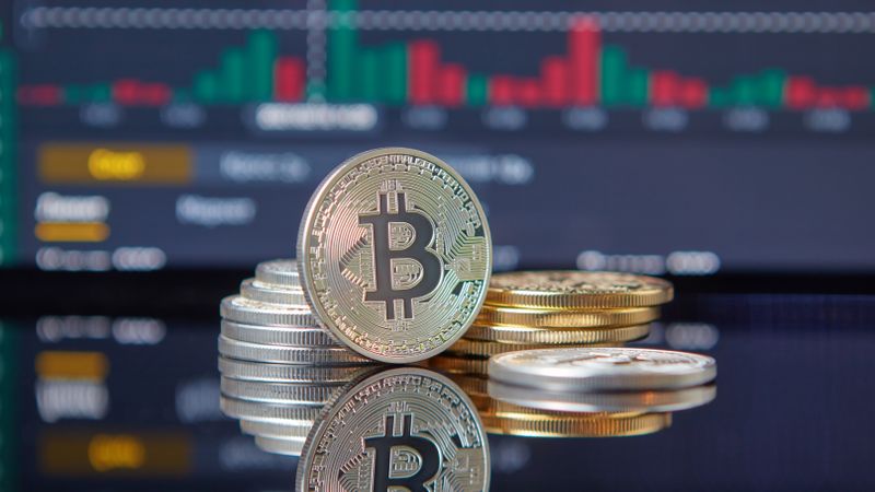 Close-up of Bitcoin coins on reflective surface with financial trading chart, symbolizing cryptocurrency market dynamics.