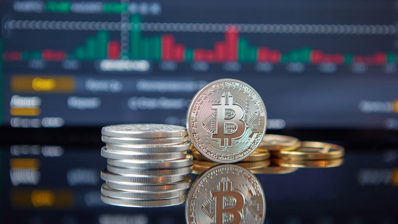 Stack of Bitcoin coins in front of a stock market graph, reflecting cryptocurrency trends.