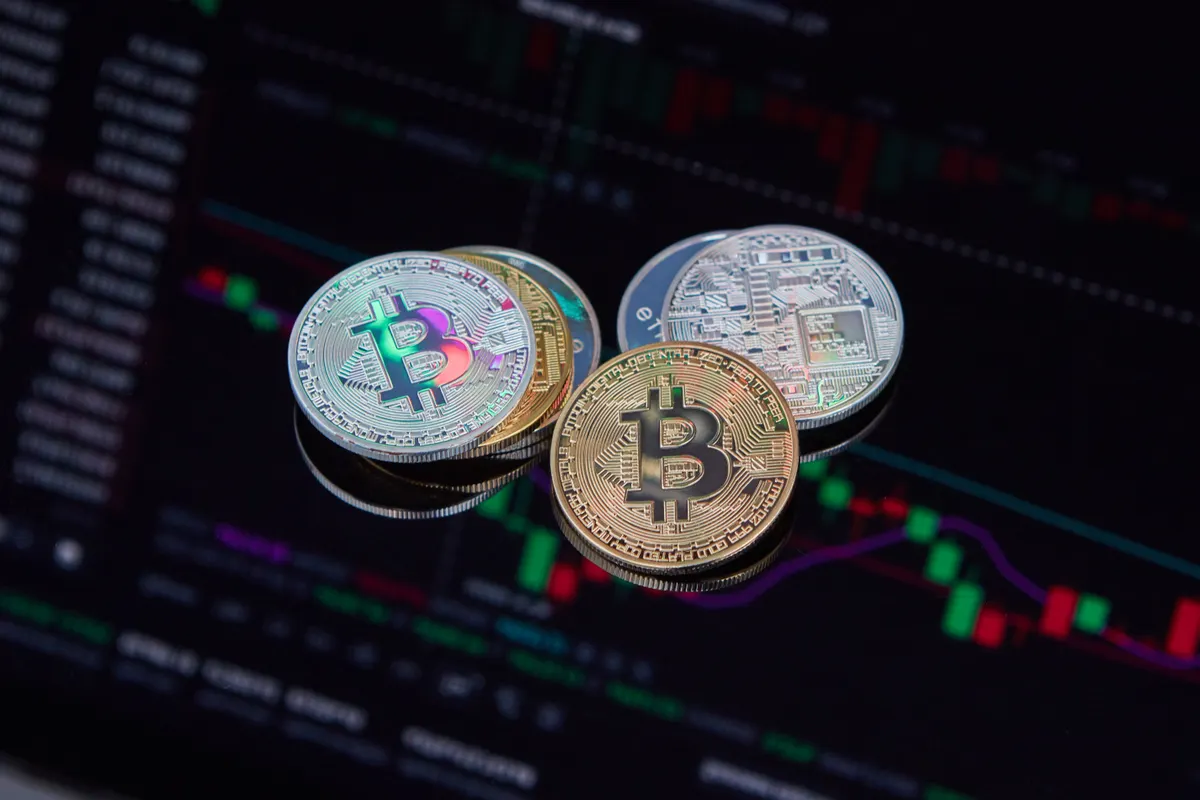 Physical Bitcoin coin resting on a screen displaying a fluctuating stock market chart, representing crypto futures volatility.