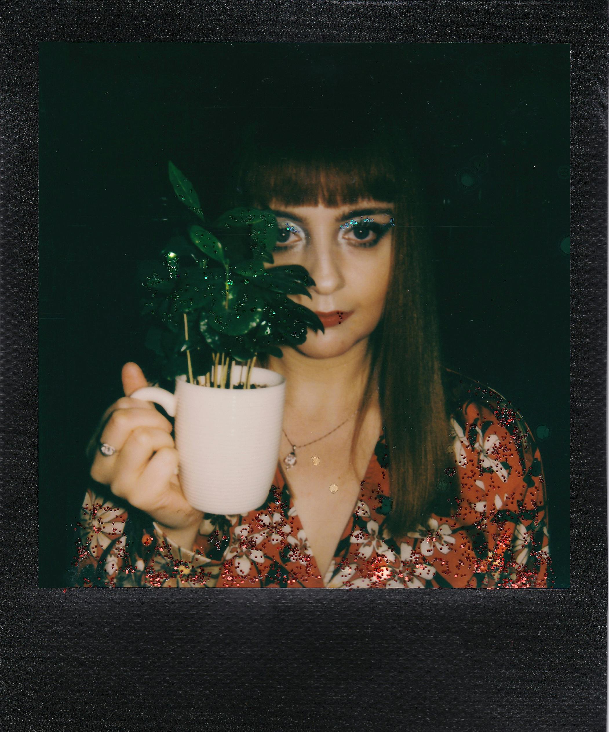 A portrait of a woman with dramatic makeup holding a plant in a mug.