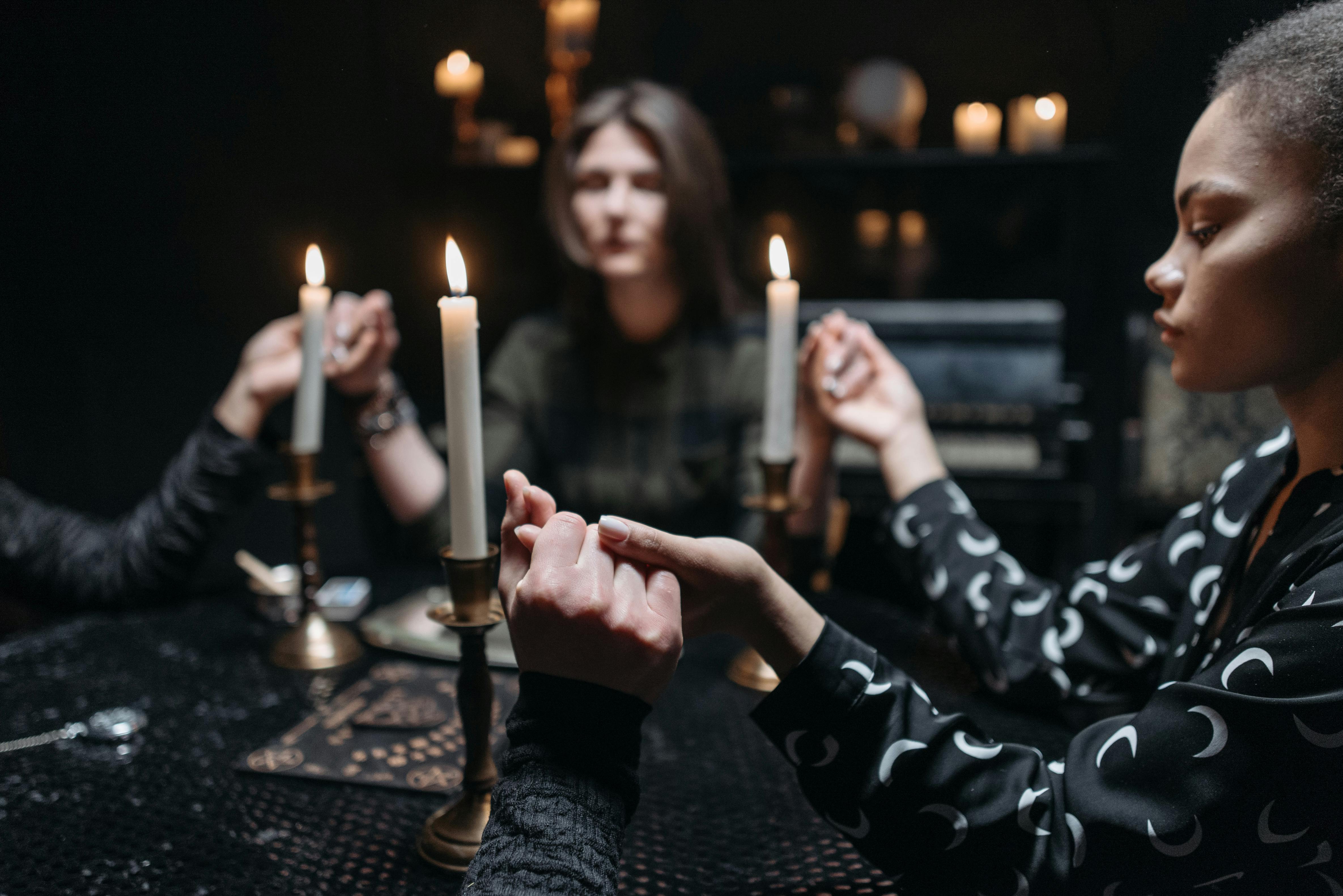 A small group of people gathered in a dimly lit room, holding hands in prayer, with a plate of food on a table nearby