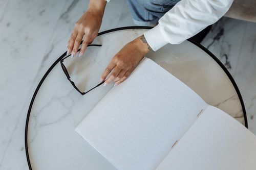 Free A person reading Braille with sunglasses and book on a table Stock Photo