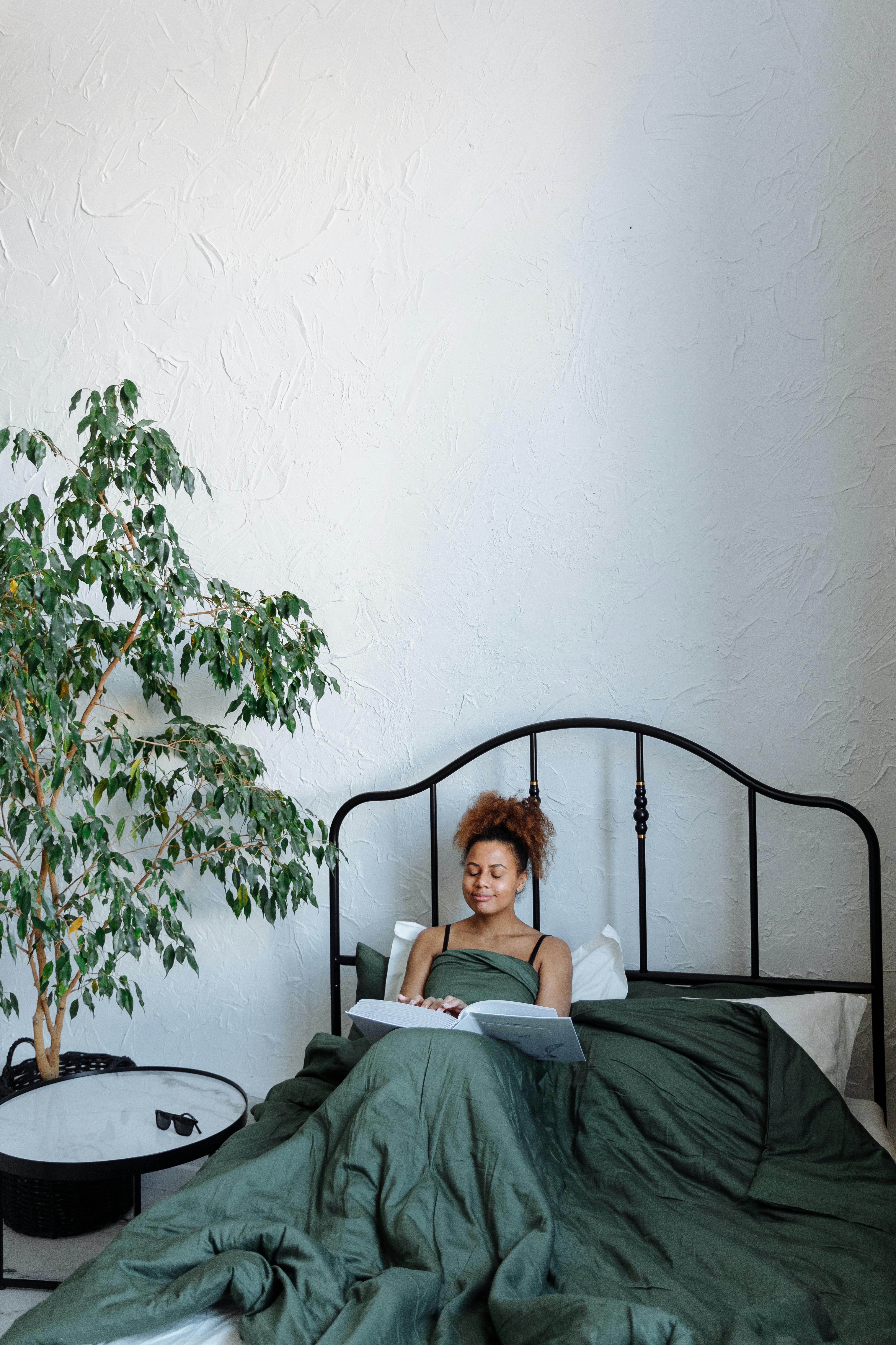African American woman reading a braille book in a cozy bedroom with a green bedspread.