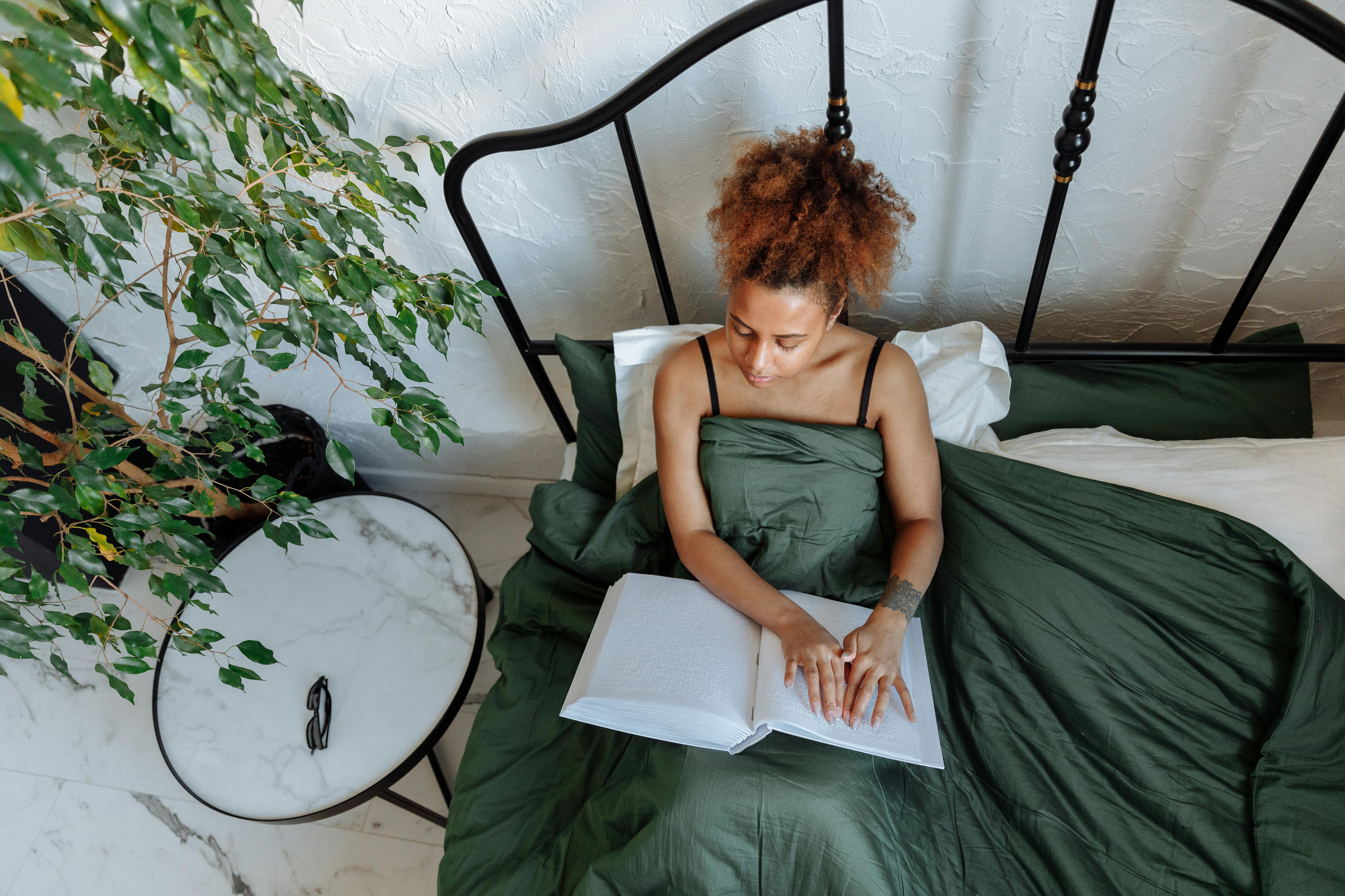 A woman sits in bed using Braille in a calm bedroom setting, highlighting inclusivity.