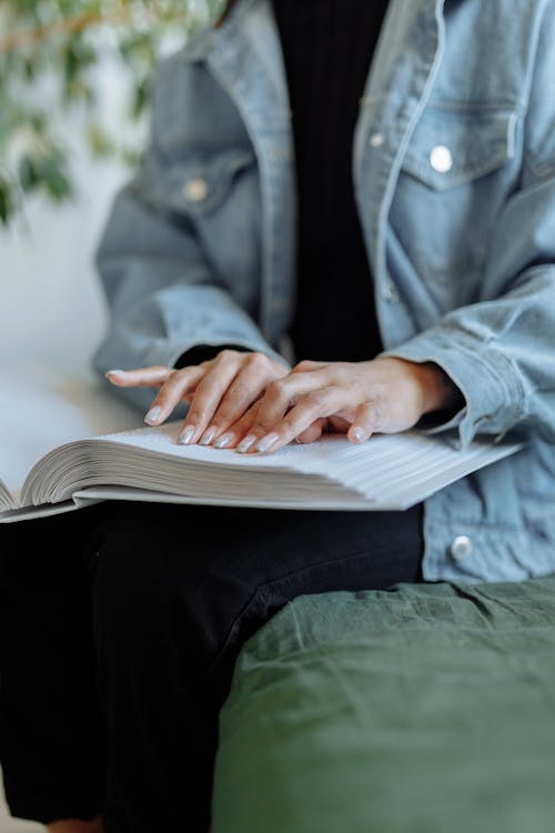 Person in Blue Denim Jacket Using a Braille