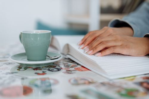 Free Close-up of a woman's hands reading a braille book while enjoying coffee, emphasizing sensory engagement. Stock Photo