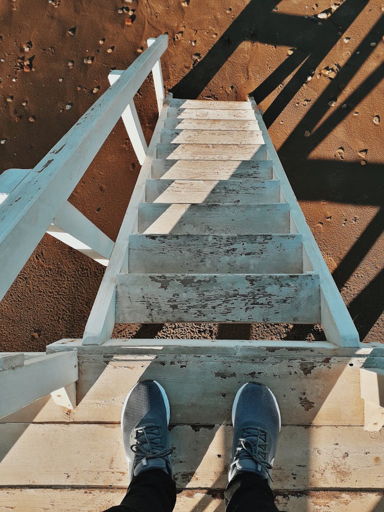 Person Standing On A Lifeguard Hut And Taking Picture Of Stairs And Sand 