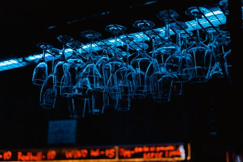 Free Racks of wine glasses hang in a dimly lit bar, illuminated by neon lights. Stock Photo