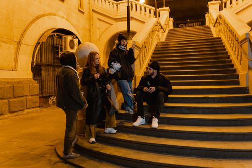 Free A group of young adults socialize on a city staircase under streetlights at night, enjoying drinks and conversation. Stock Photo