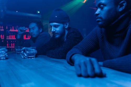 Free Three men enjoying a drink at a dimly lit nightclub bar, showcasing nightlife and friendship. Stock Photo
