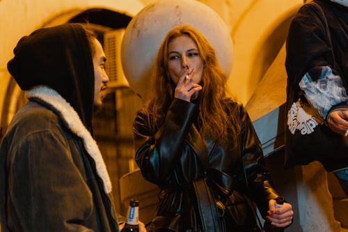Free Group of friends enjoying a night out, smoking and drinking in an urban setting. Stock Photo
