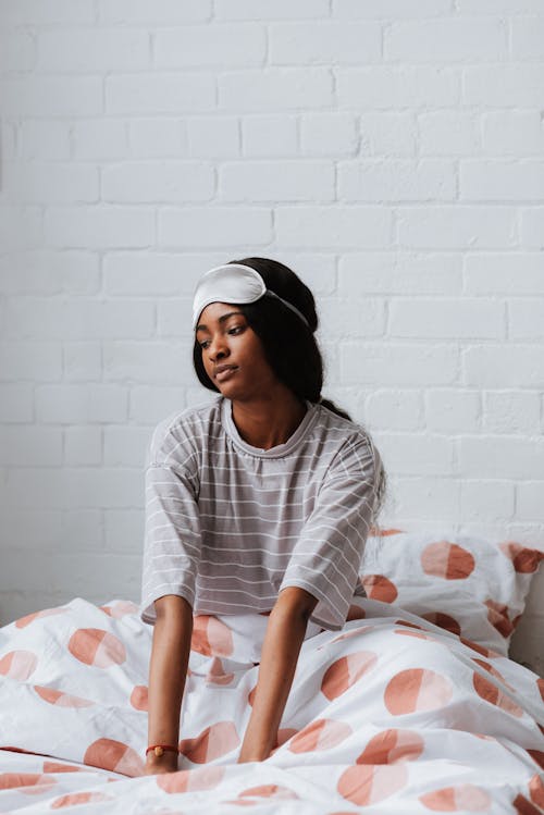 Free A Woman in Striped Shirt Sitting on Her Bed with Sleeping Mask on Her Head Stock Photo