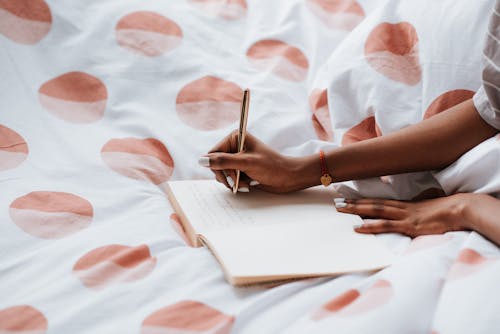 Close-up of Woman Writing in Notebook in Bed