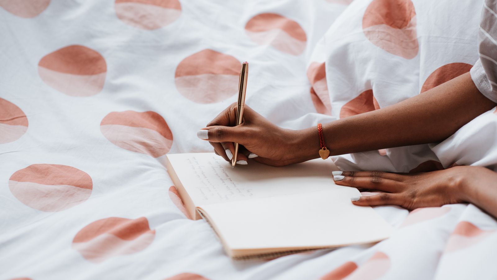 A woman writing in a notebook while sitting on a bed with polka-dot sheets