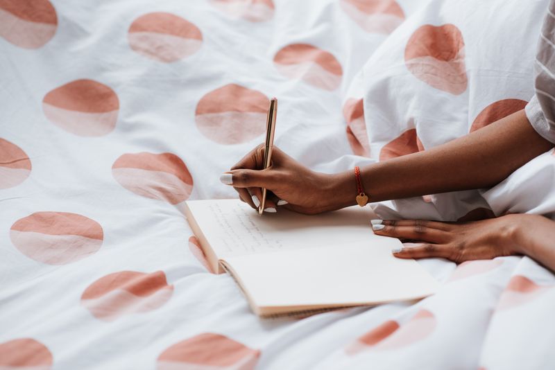 A woman journaling on a bed with polka dot sheets, creating a cozy atmosphere.