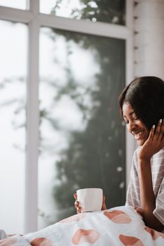 A joyful woman with a ceramic cup sitting by a window with natural light.