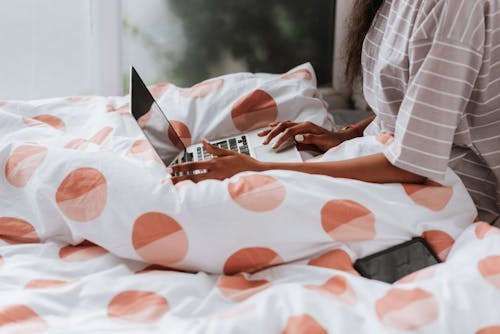 Free A Person in Striped Shirt Sitting on the Bed while Using a Laptop Stock Photo