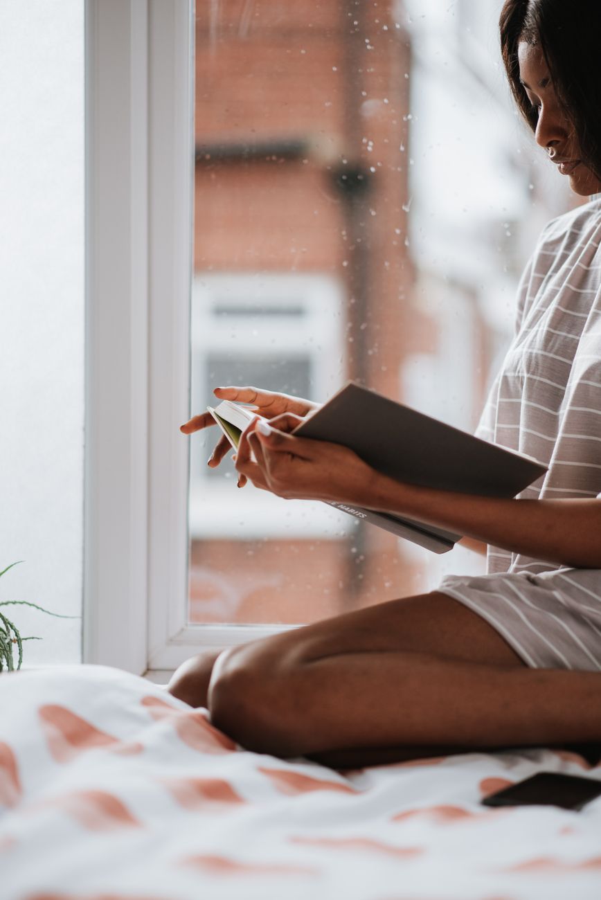 A woman enjoys reading a book by the window, embracing a tranquil rainy day indoors.. woman, enjoys, reading