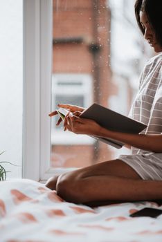 A woman enjoys reading a book by the window, embracing a tranquil rainy day indoors.. woman, enjoys, reading
