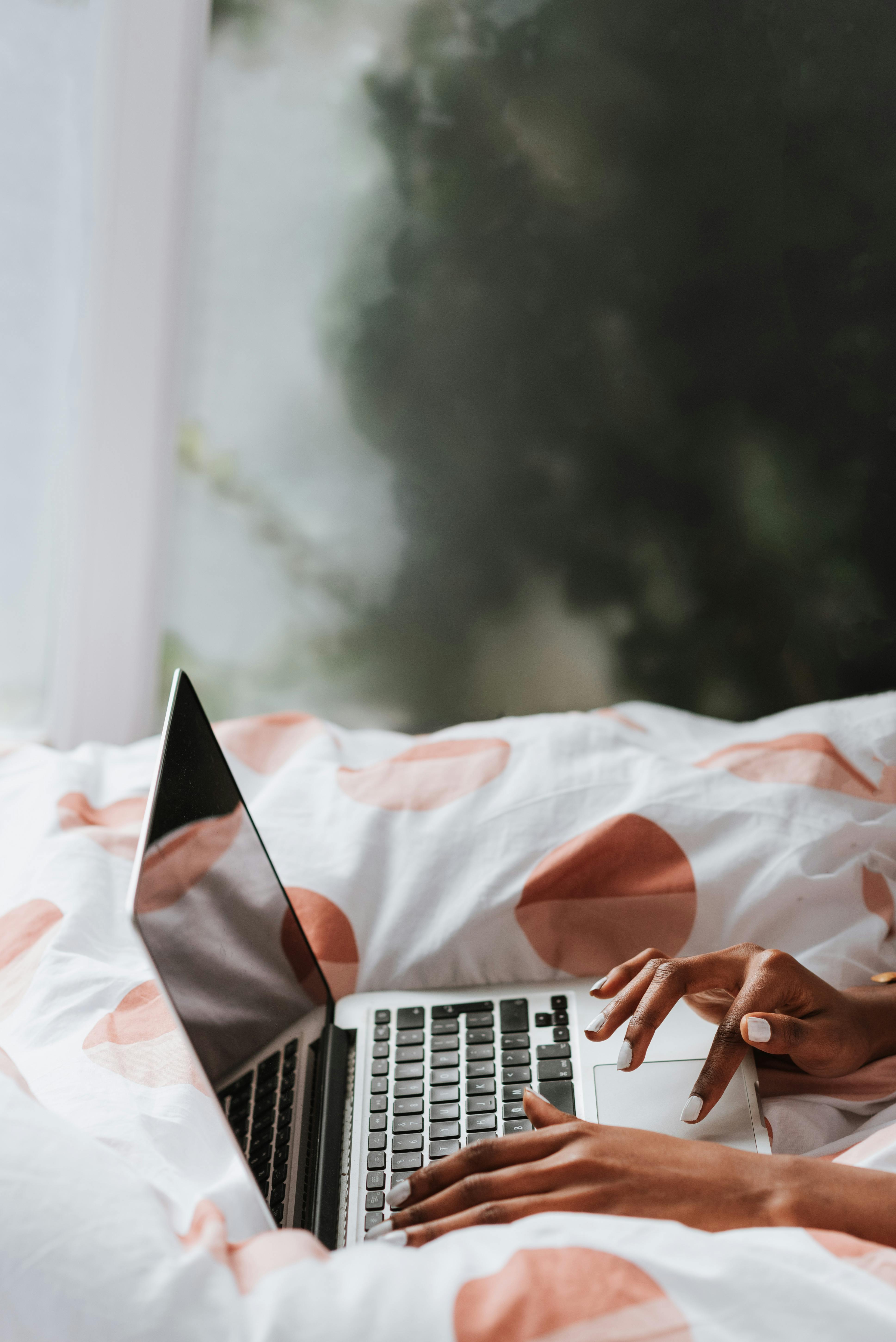 A woman uses a laptop while sitting on a bed with polka dot sheets, offering a cozy work-from-home vibe.