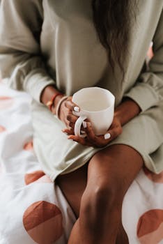 Close-up of a woman holding a coffee cup while sitting comfortably indoors.