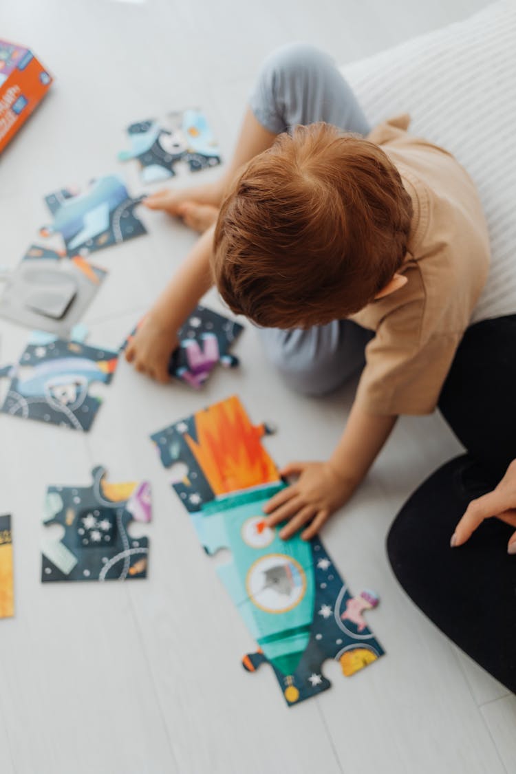 Overhead Shot Of A Boy In A Brown Shirt Solving A Jigsaw Puzzle