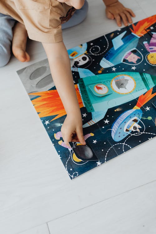 Photo of a Child in a Brown Shirt Solving a Jigsaw Puzzle