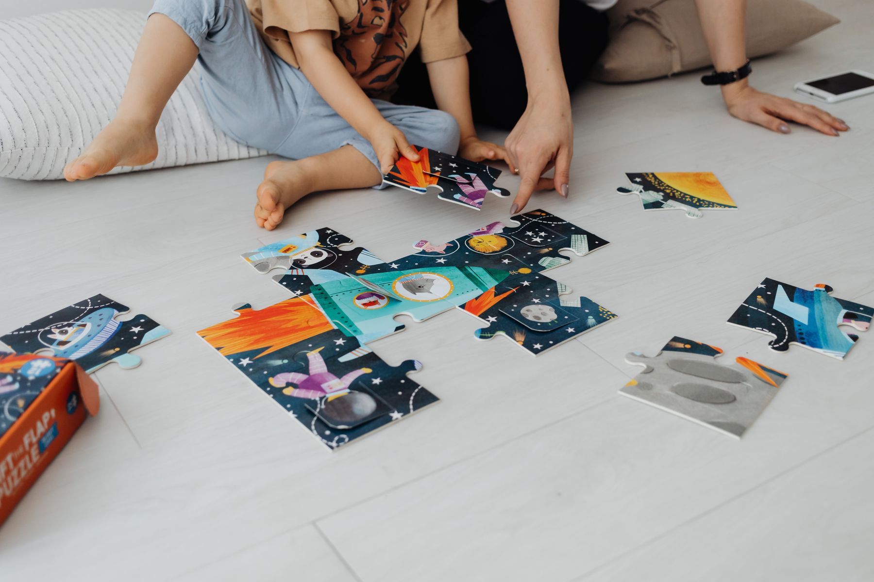 A child and caregiver assembling a large space-themed educational puzzle together on a bright floor