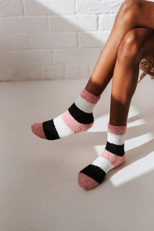 Free Crop unrecognizable ethnic female in soft socks sitting with crossed legs against brick wall at home in sunlight Stock Photo