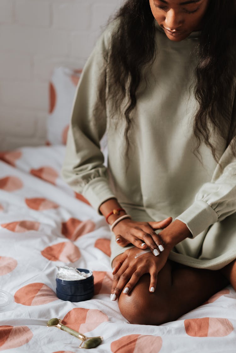 Crop Black Woman Applying Hydrating Cream On Hand In Bedroom