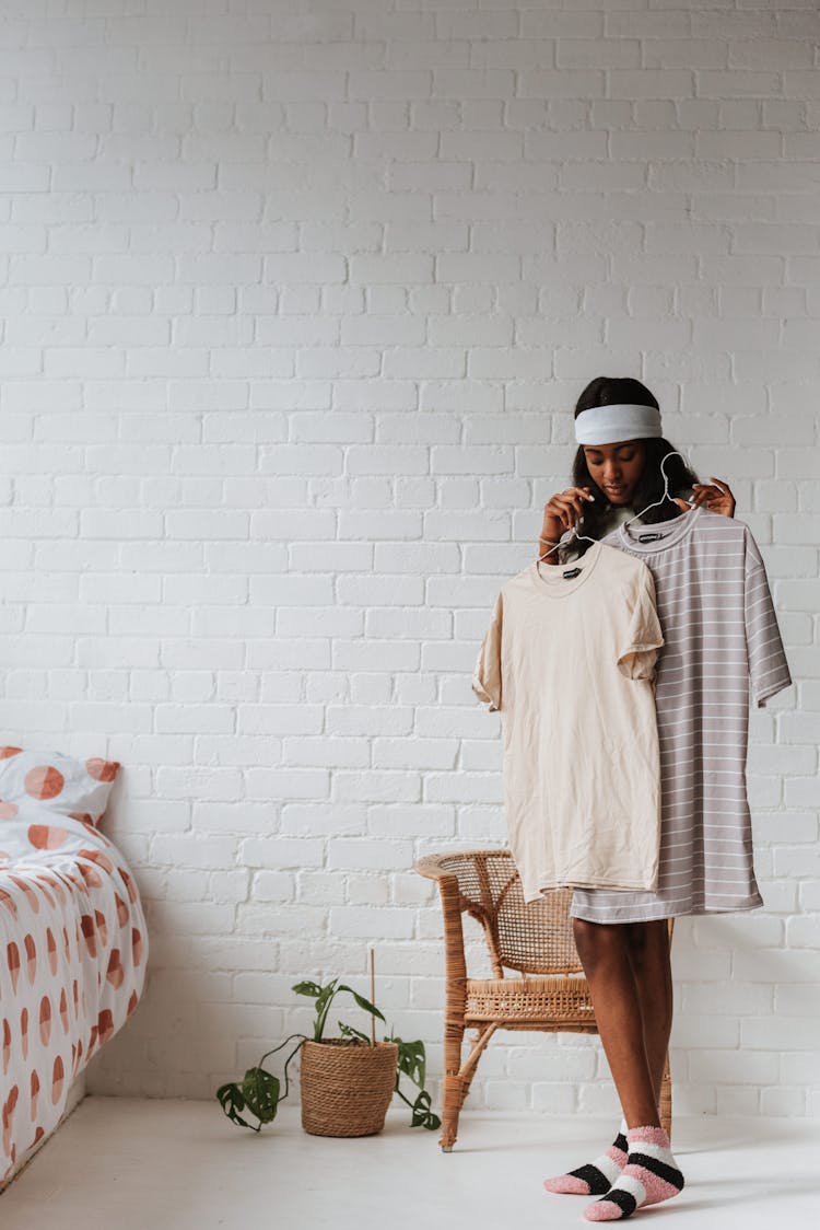 Ethnic Woman Choosing T Shirt In Bedroom On White Background