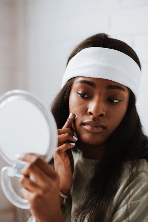 African American woman with mirror applying nourishing cream on face