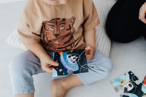 Free A young child sits on the floor assembling a space-themed puzzle piece. Stock Photo
