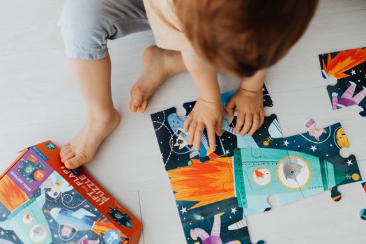 Top view of a child assembling a colorful space-themed puzzle indoors.