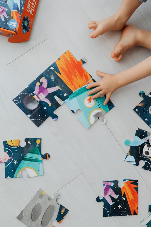 Free A child playing with a colorful space-themed jigsaw puzzle, showing hands and feet on a light floor. Stock Photo